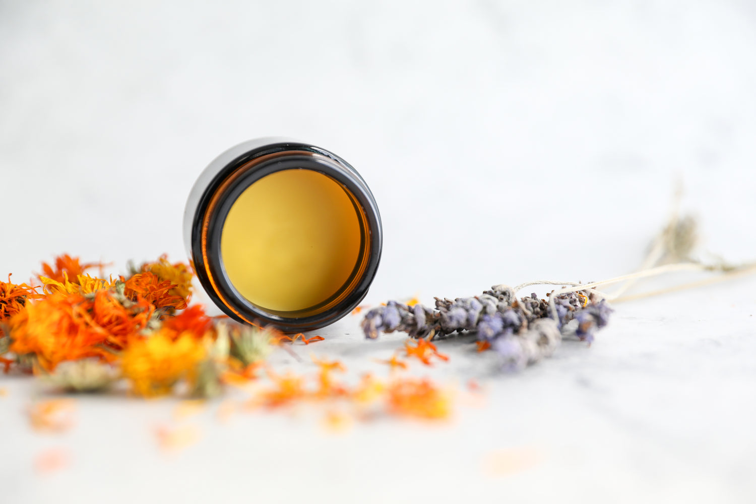 Open jar of calendula salve with dried flowers of calendula and lavender